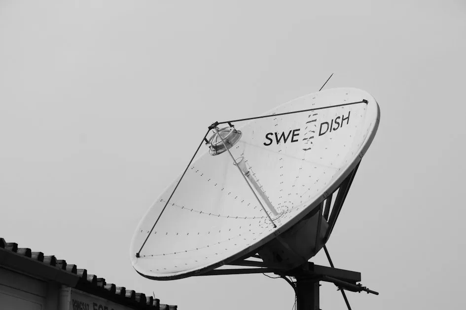 A white satellite dish with the text "SWE DISH" against a grey sky